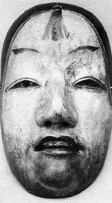 Soluk yüzlü, dudakları kapalı, sakin ifadeli bir Japon Noh tiyatrosu maskesi; siyah beyaz fotoğraf.
